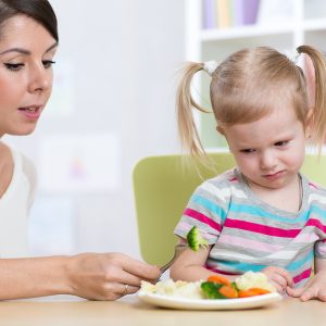 Child Girl Looks With Disgust At Healthy Vegetables. Mother Conv