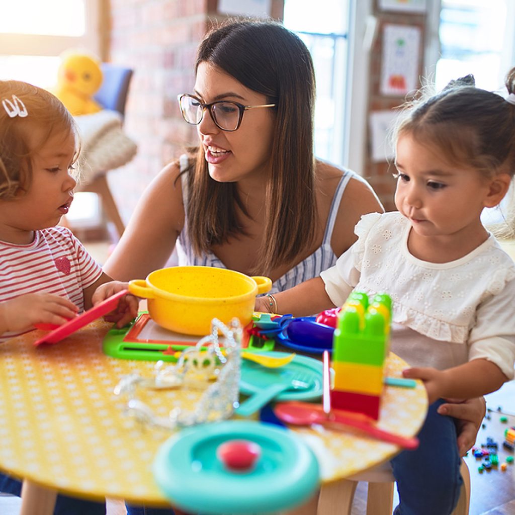 Young Beautiful Teacher And Toddlers Playing Meals Using Plastic