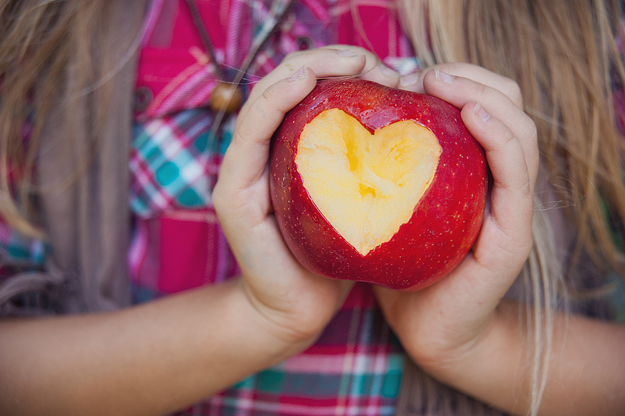girl holding a ripe apple with heart shaped cutout. girl eating